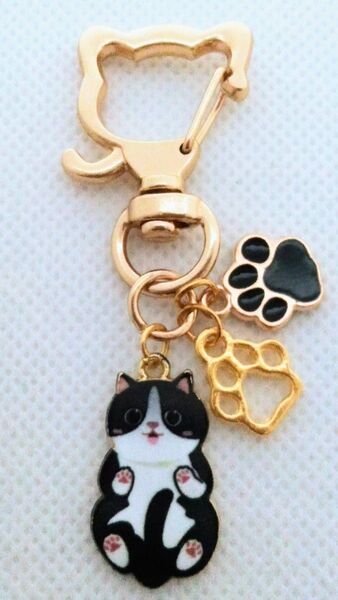 黒色とゴールドの肉球とゴロンとへそ天する黒ハチワレの猫キーホルダー