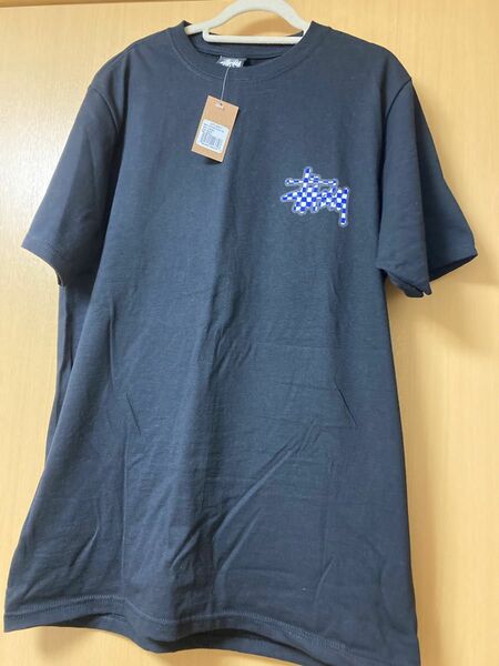 ステューシーのTシャツSサイズです。色は黒。青×白の千鳥格子柄のステューシーロゴマークになってます。新品未使用タグ付き。